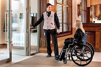 Recepcionista abre puerta a usuario de silla de rueda